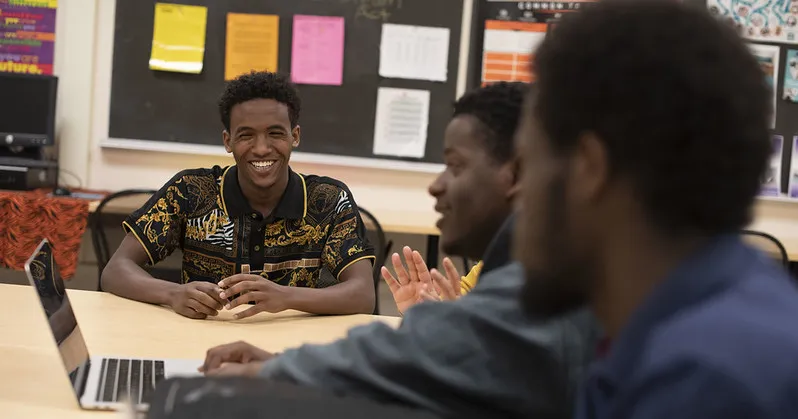 Three students sitting together at a classroom table and laughing. 