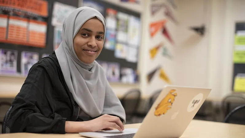 Student working at table in school with laptop 