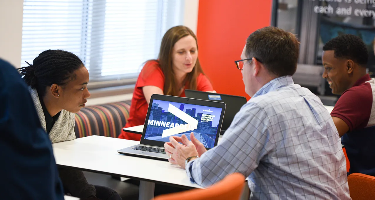 Adult and interns sitting together at table looking at laptop screen