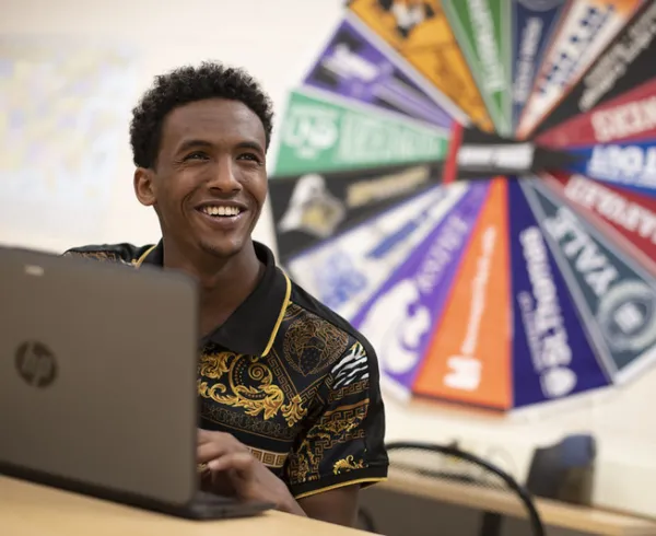 Student with laptop sitting in front of college pennants.