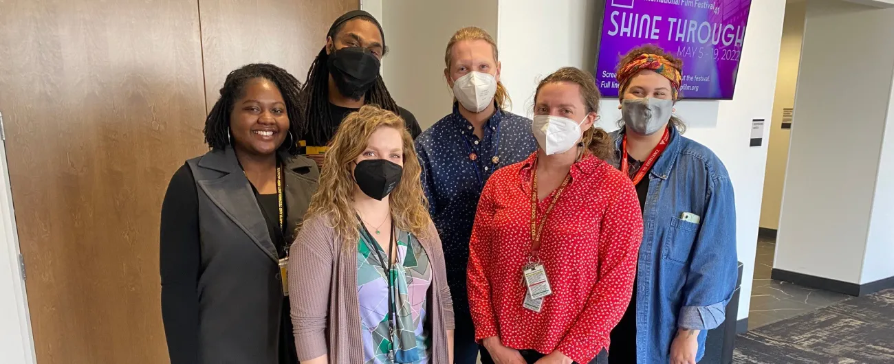 Six people with masks smiling at the camera in a hallway