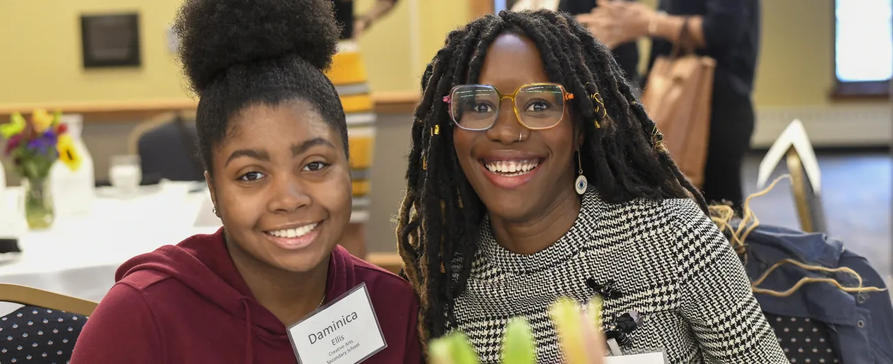 High school student and adult staff sitting at event table and smiling at the camera