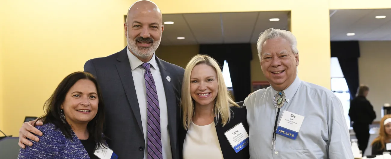 Four people standing together smiling at the camera