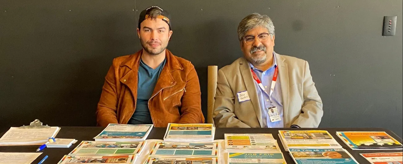 Two men at Takota Institute display table smiling at the camera