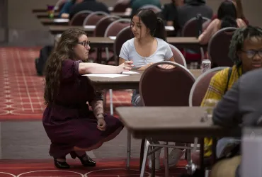 Local professional crouches next to a young person to provide feedback on their resume